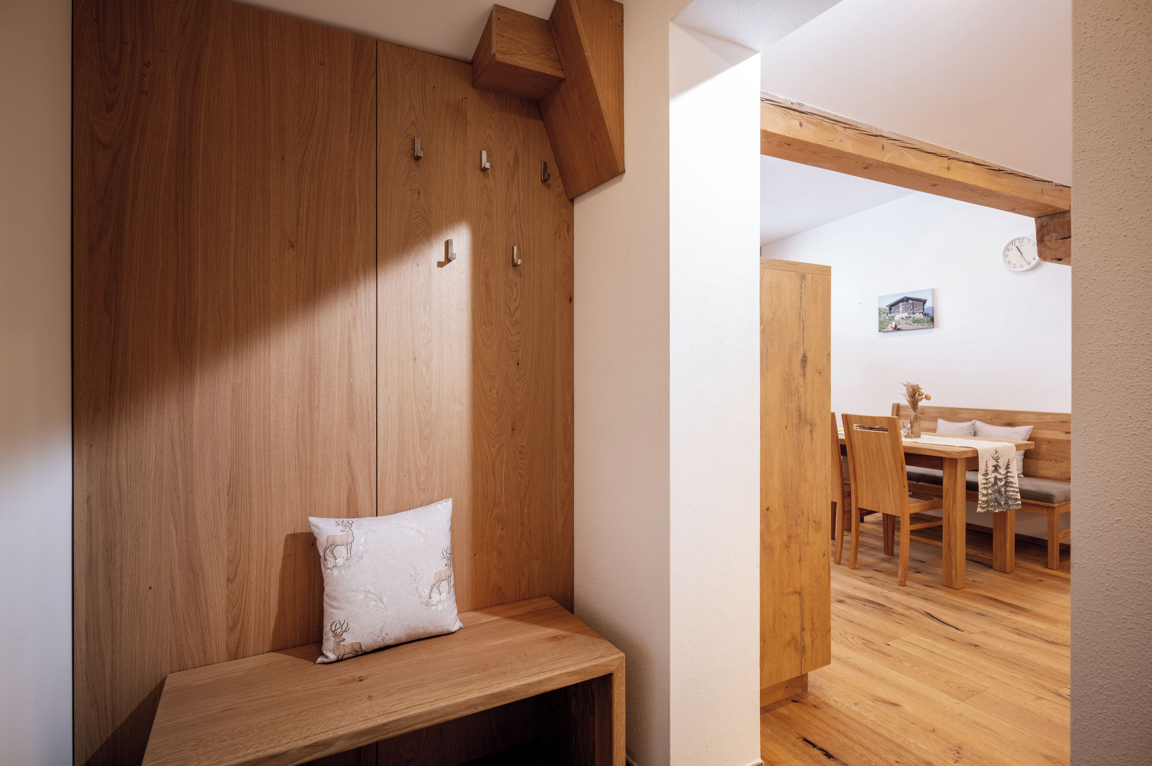 Un banco de madera con cojín, una pared de madera con ganchos y un comedor con mesa y sillas.