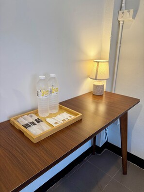 A wooden table with a tray containing two bottles and packets, a lamp, and a power outlet on the wall. - Zzz at Nimman : 3 Floors Cafe Townhouse with Rooftop View (Suthep)