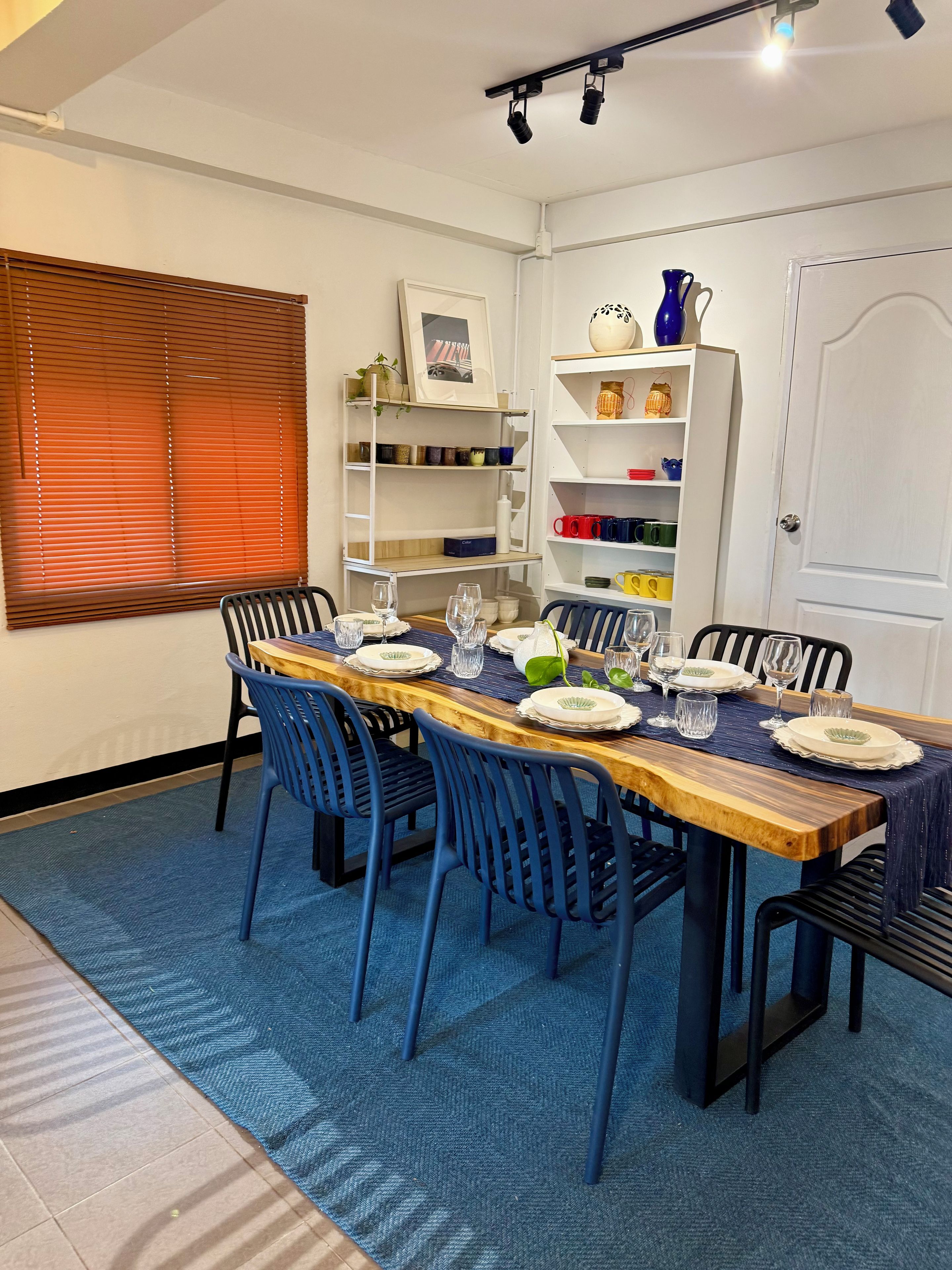 Uma sala de jantar com uma mesa de madeira comprida posta para seis pessoas, rodeada por cadeiras azuis.