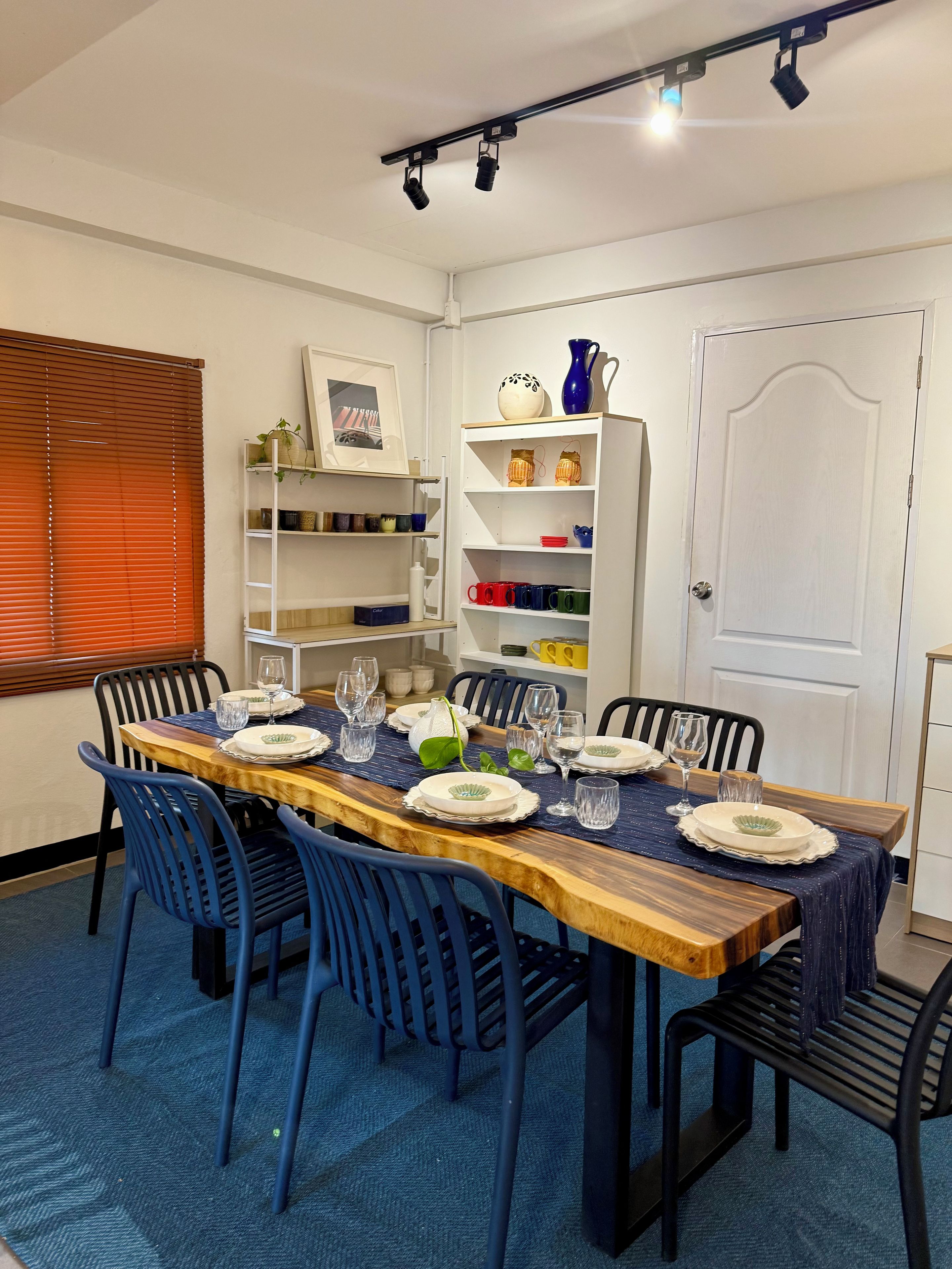 A dining room with a wooden table set for six, blue chairs, and a white door in the background.