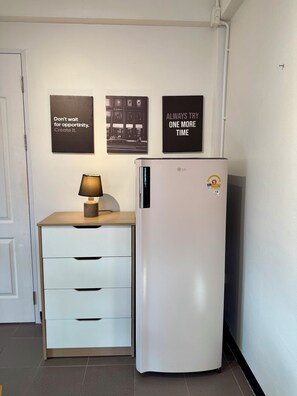 A kitchenette with a white refrigerator, a wooden cabinet with drawers, a lamp on the cabinet, and motivational posters on the wall. - Zzz at Nimman : 3 Floors Cafe Townhouse with Rooftop View (Suthep)