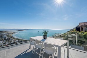 A terrace with a white table and chairs overlooking a coastal view. - The Coastal Haven Villa (Christchurch)