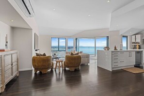 A spacious living area with a view of the sea, a kitchen with white cabinets, and a dining area with a table and chairs. - The Coastal Haven Villa (Christchurch)