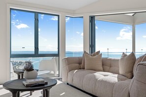 A modern living room with a large sofa, a coffee table, and a view of the sea. - The Coastal Haven Villa (Christchurch)