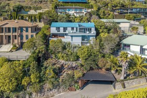 A modern two-story house with a flat roof, surrounded by lush greenery and a paved driveway. - The Coastal Haven Villa (Christchurch)