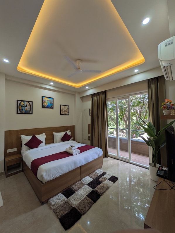 A modern hotel room with a large bed, ceiling fan, recessed lighting, and a view of the outdoors. - The Lodgers Service Apartment Sector 42 (Gurugram)