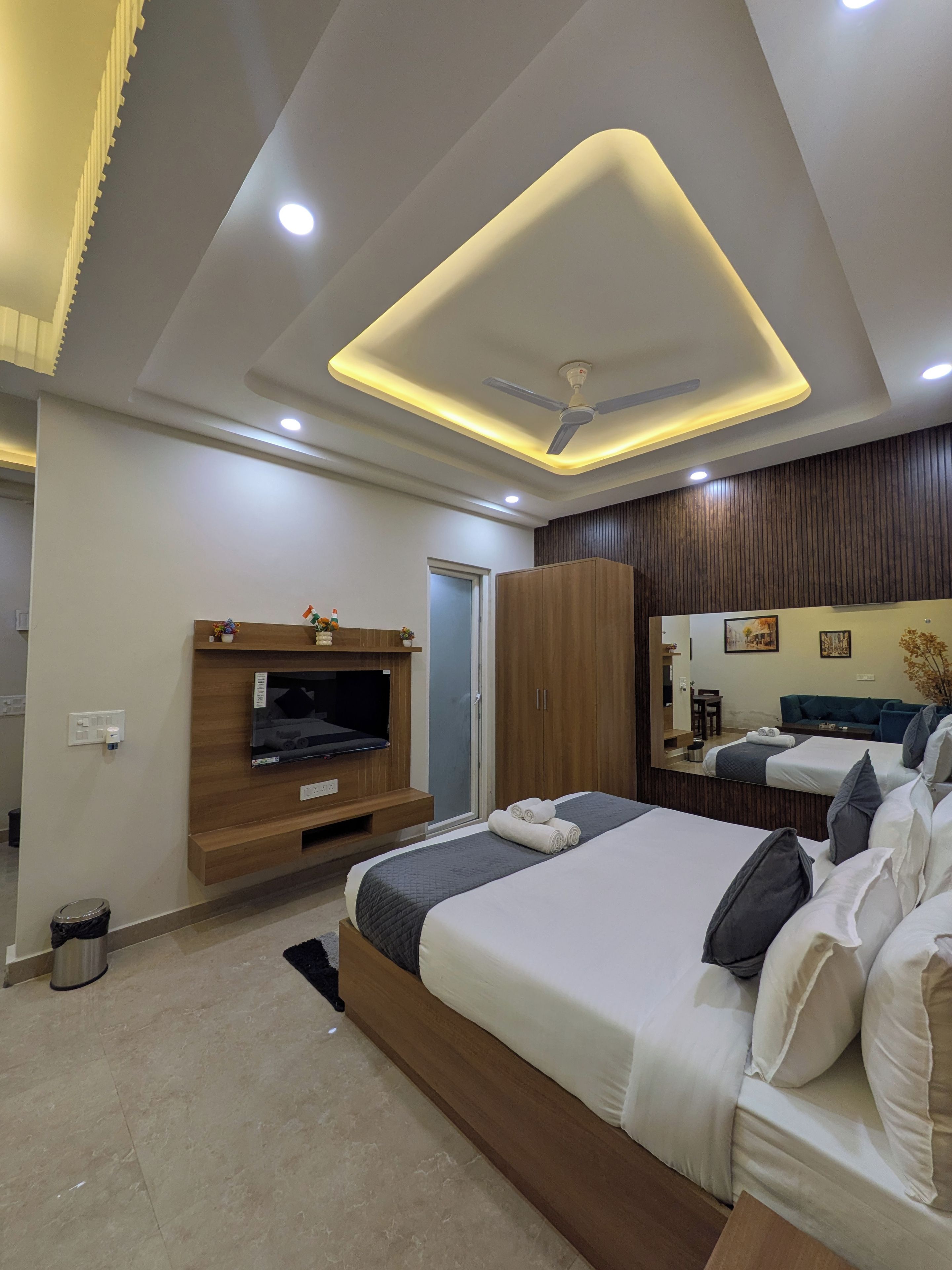 A modern bedroom with a bed, a TV, a wardrobe, and a mirror.