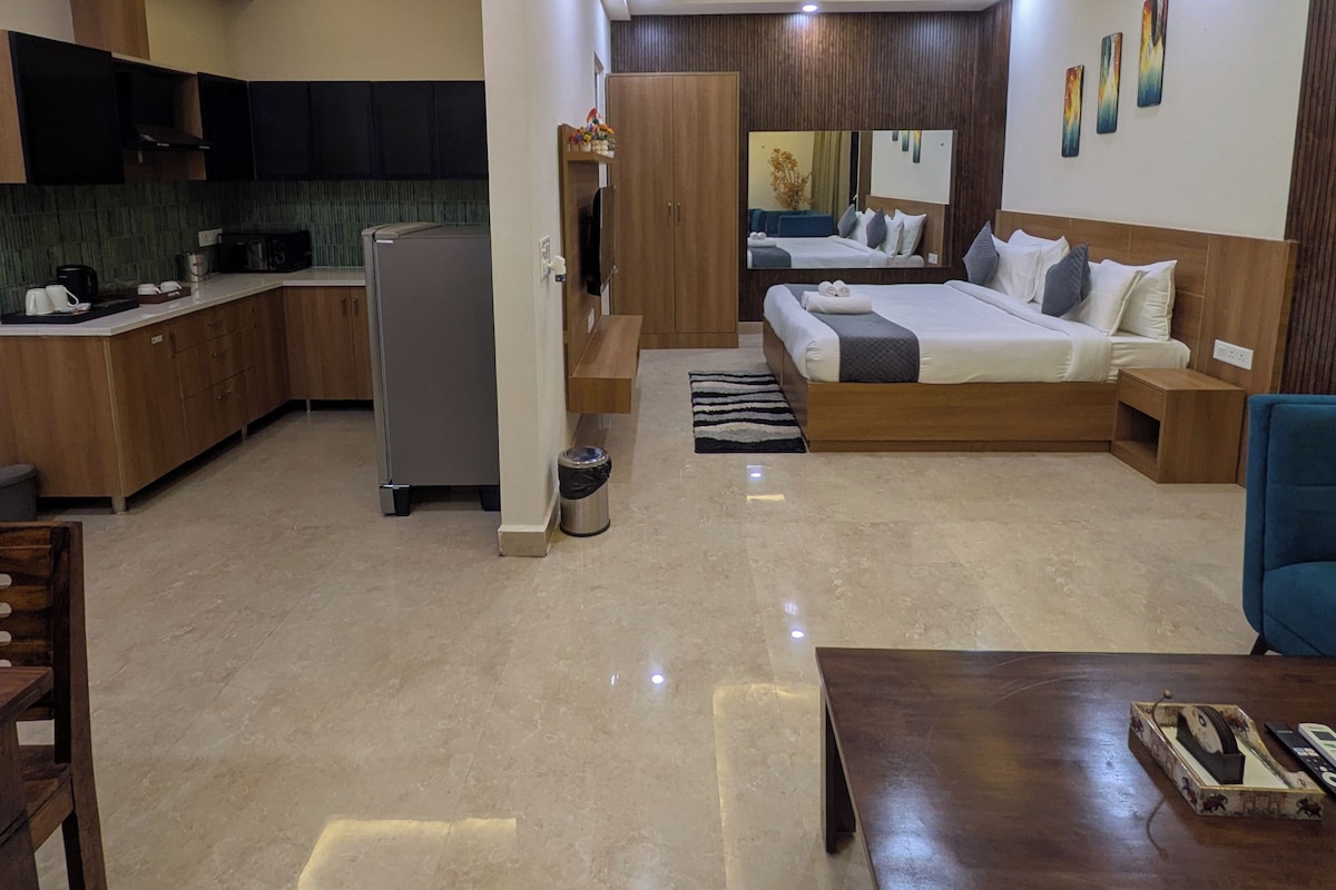 A modern hotel room with a bed, seating area, kitchenette, and a bathroom.