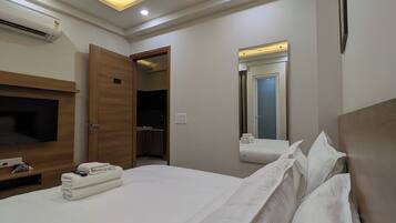 A hotel room with a bed, a TV, an air conditioner, a ceiling fan, and a mirror.