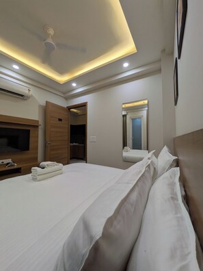 Una habitación de hotel con cama, televisor, aire acondicionado, ventilador de techo y espejo.