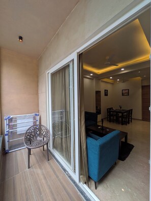 A modern living room with a blue sofa, a dining table with chairs, and a glass door leading to a balcony. - The Lodgers Service Apartment Sector 42 (Gurugram)