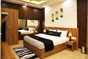 Quarto de hotel moderno com uma cama grande, televisão, guarda-roupa de madeira e espelho.