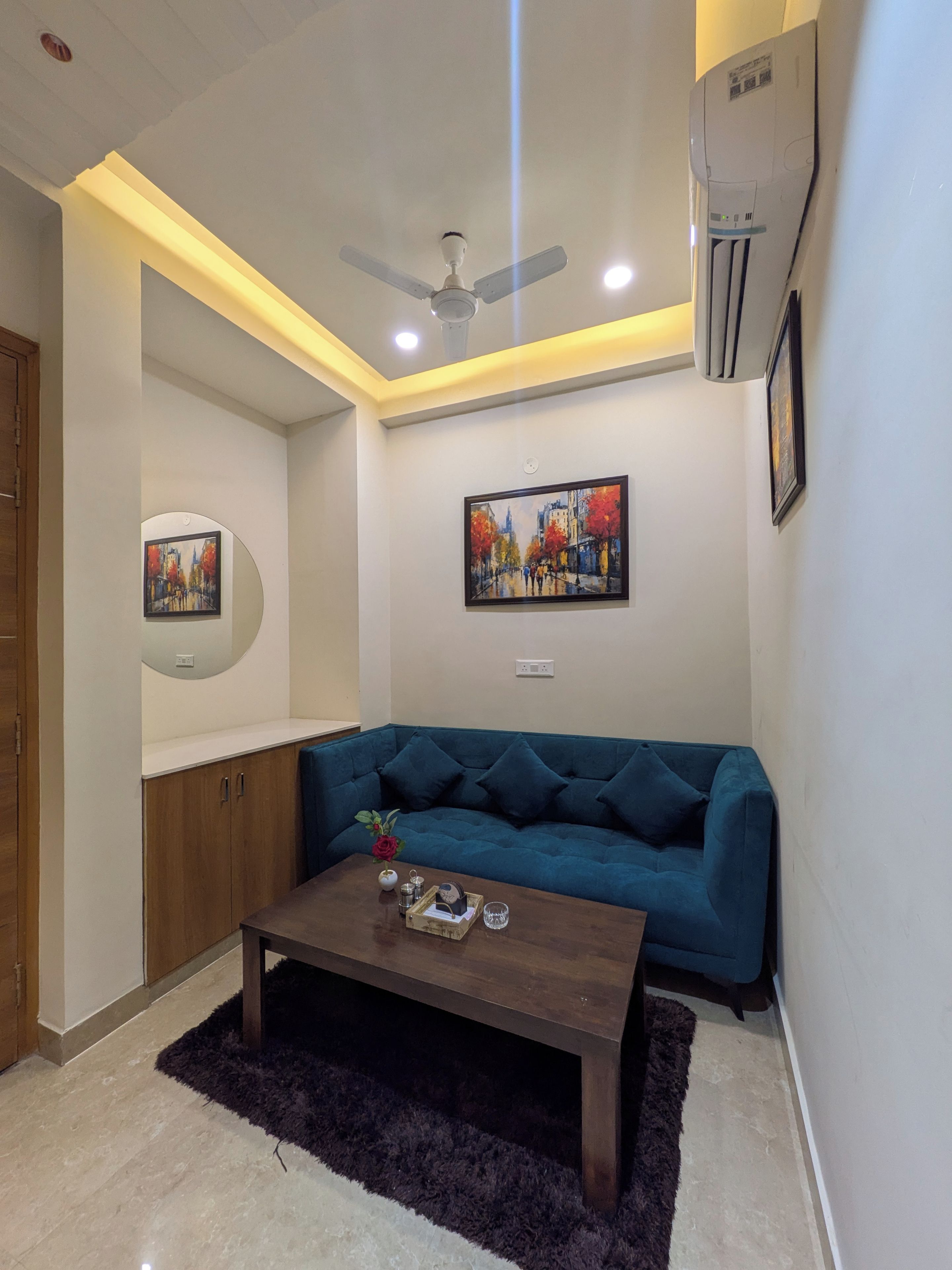 A living room with a blue sofa, a coffee table, a ceiling fan, and a painting on the wall.