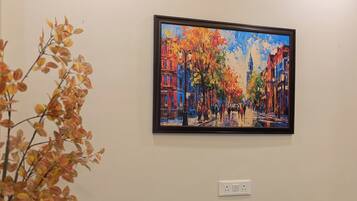A room with a blue sofa, a painting of a colorful street scene, and a plant with autumn leaves.