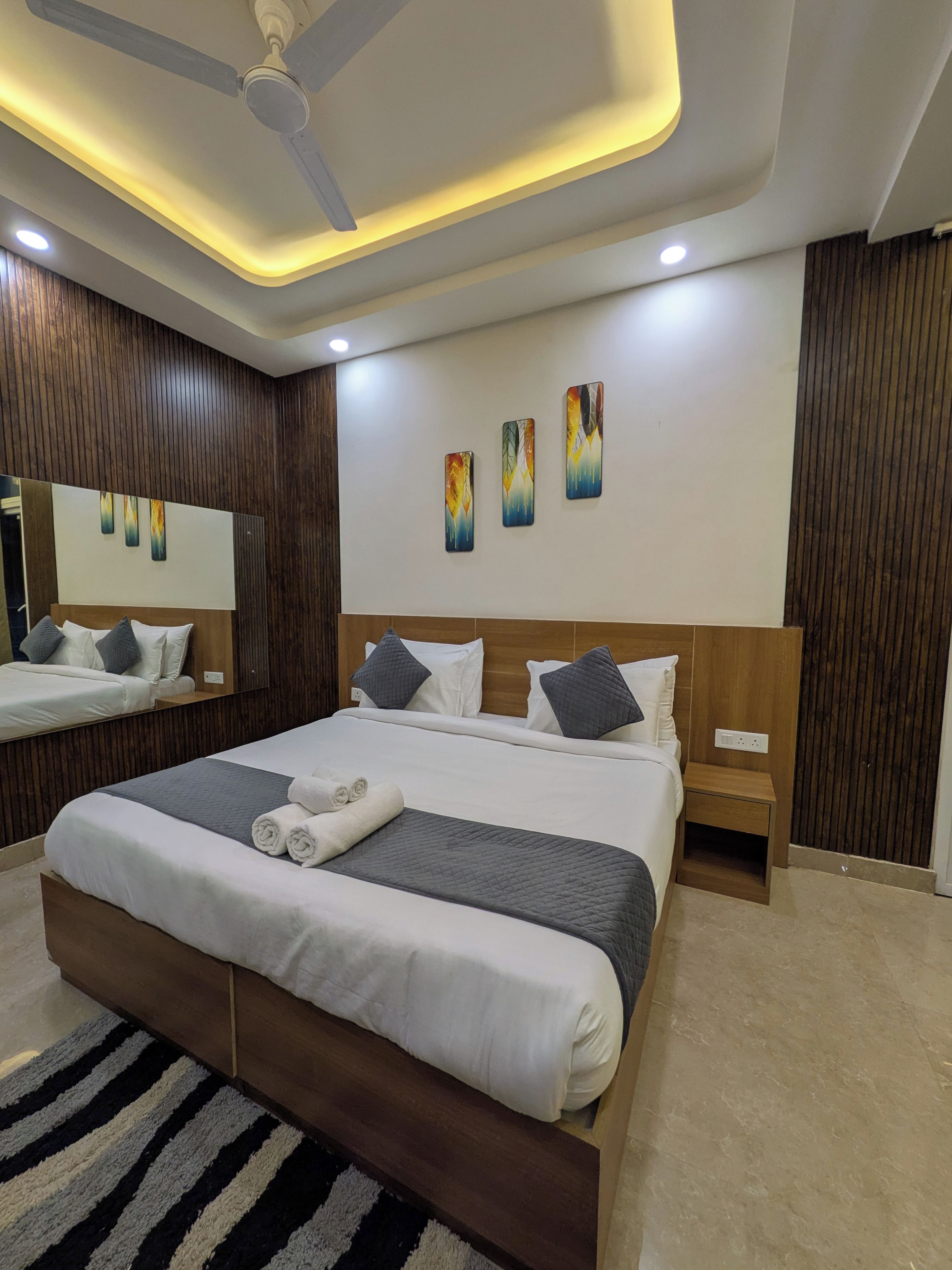 Un dormitorio moderno con una cama grande, mesitas de noche, ventilador de techo y una obra de arte en la pared.