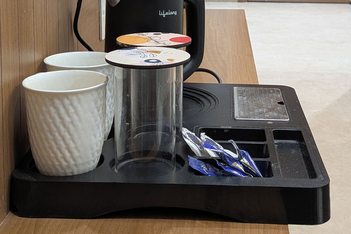 Una cafetera con una bandeja, dos tazas y un vaso sobre una mesa de madera.