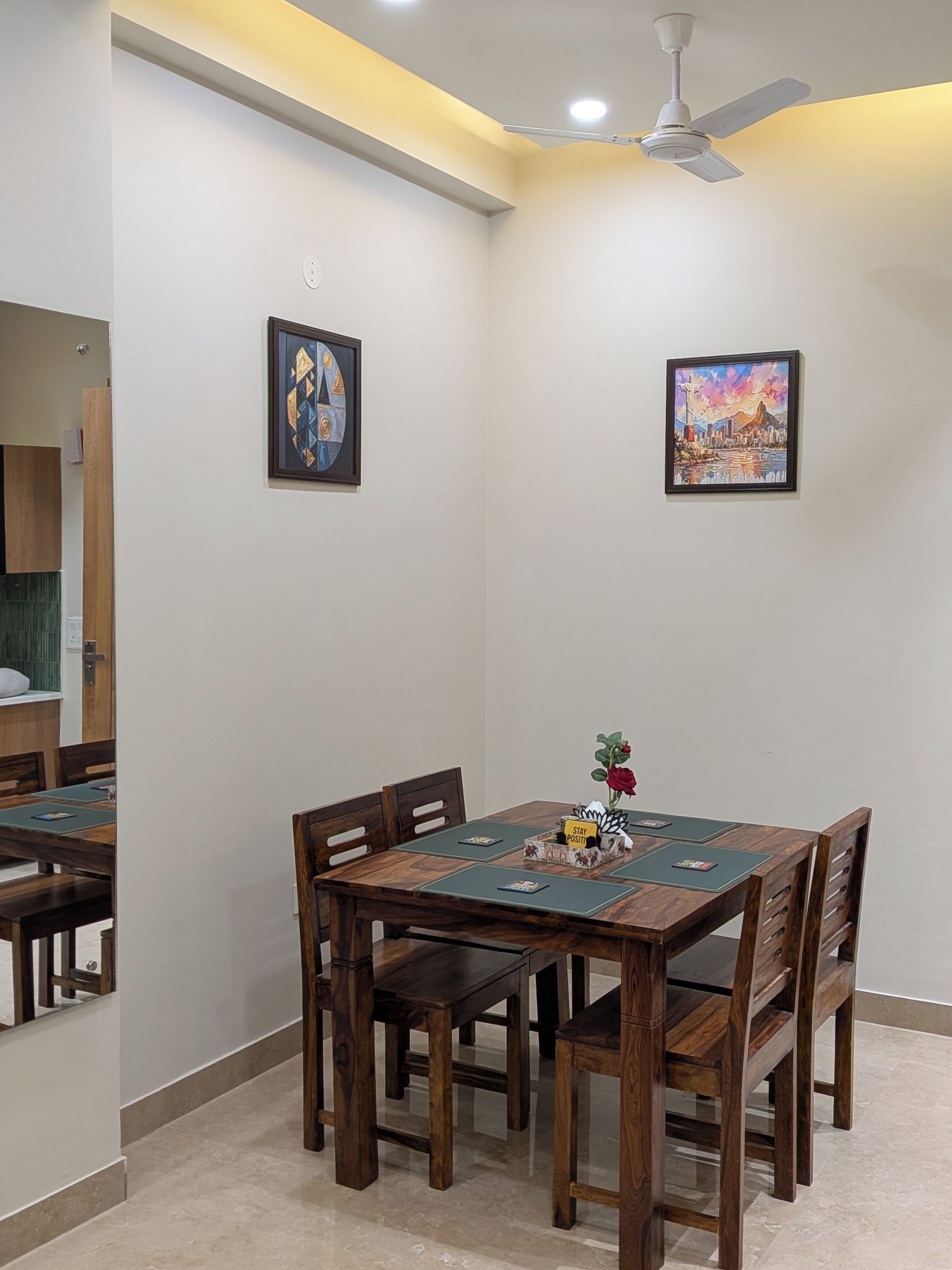 Un coin repas avec une table et des chaises, un ventilateur de plafond et deux œuvres d’art encadrées accrochées aux murs.