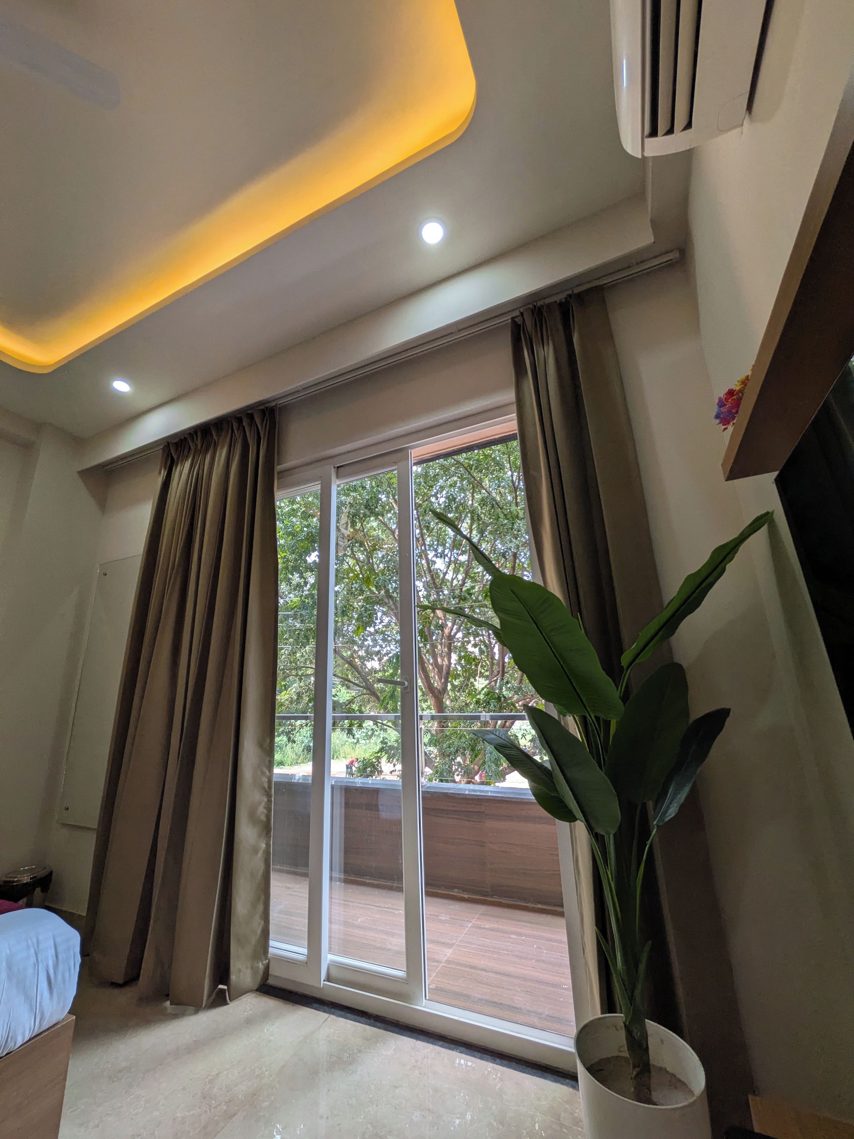 A hotel room with a large sliding glass door, a potted plant, and a ceiling with recessed lighting.