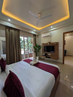 A hotel room with a bed, curtains, a ceiling fan, an air conditioning unit, a television, and a potted plant. - The Lodgers Service Apartment Sector 42 (Gurugram)