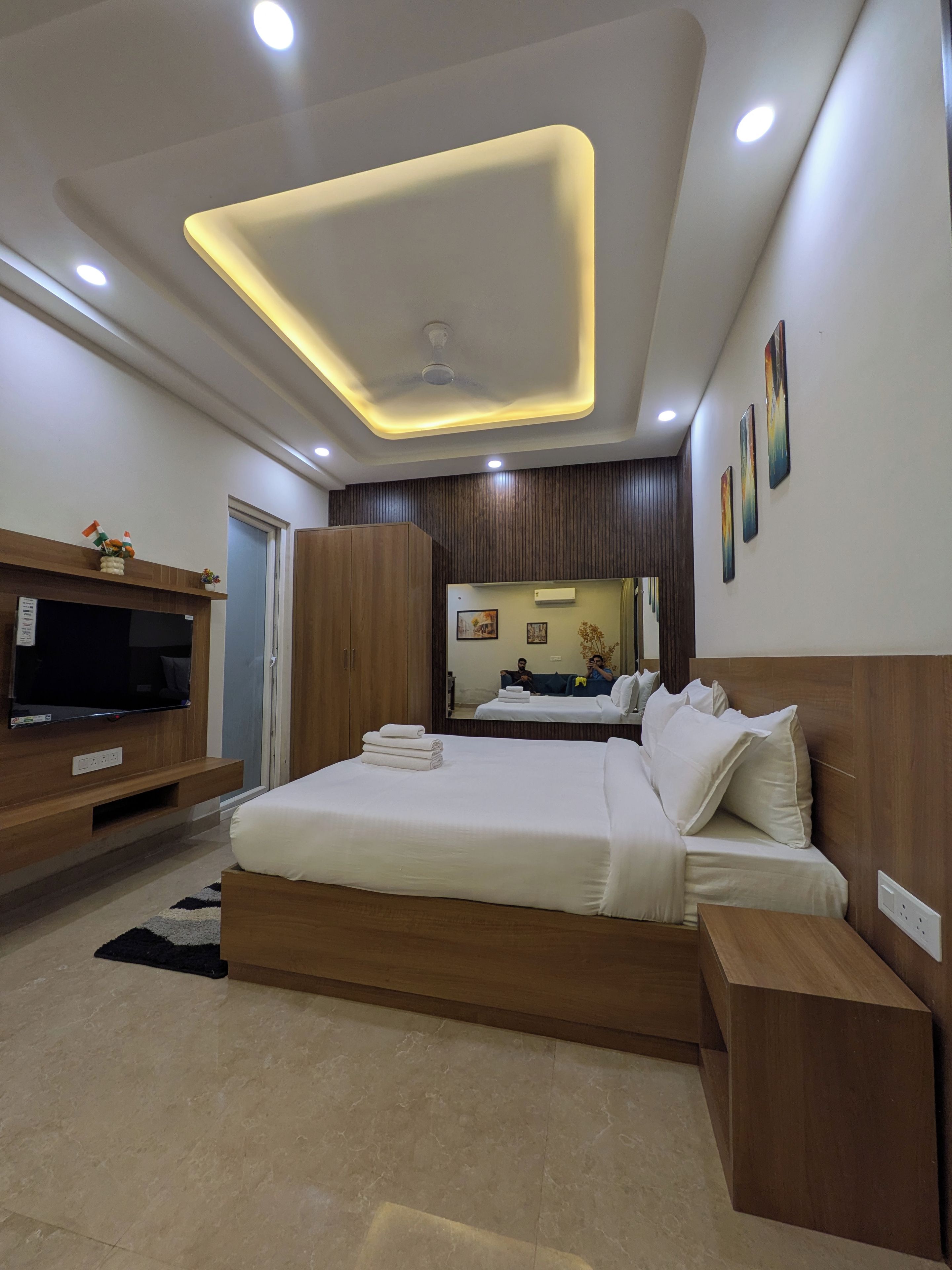 Een moderne slaapkamer met een groot bed, een flatscreen televisie, houten meubels en een plafond met inbouwverlichting.