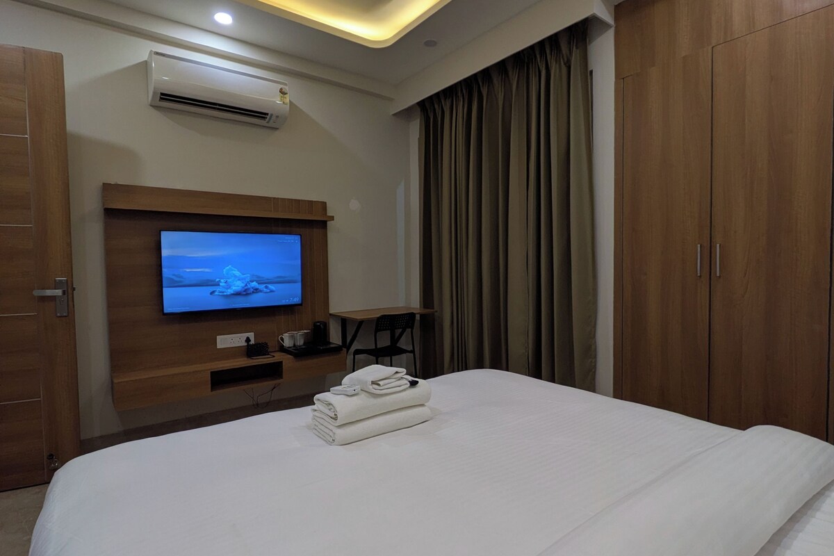 Quarto de hotel com cama, televisão na parede, ventoinha no teto e guarda-roupa.