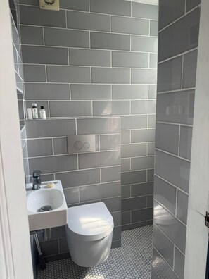 A bathroom with grey tiled walls, a white sink, and a toilet. - Room-hidden Garden Retreat En-suite Priv (Brighton)