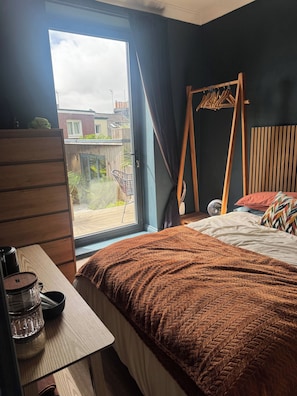 A bedroom with a bed, a wooden dresser, a window with curtains, and a view of the outside.