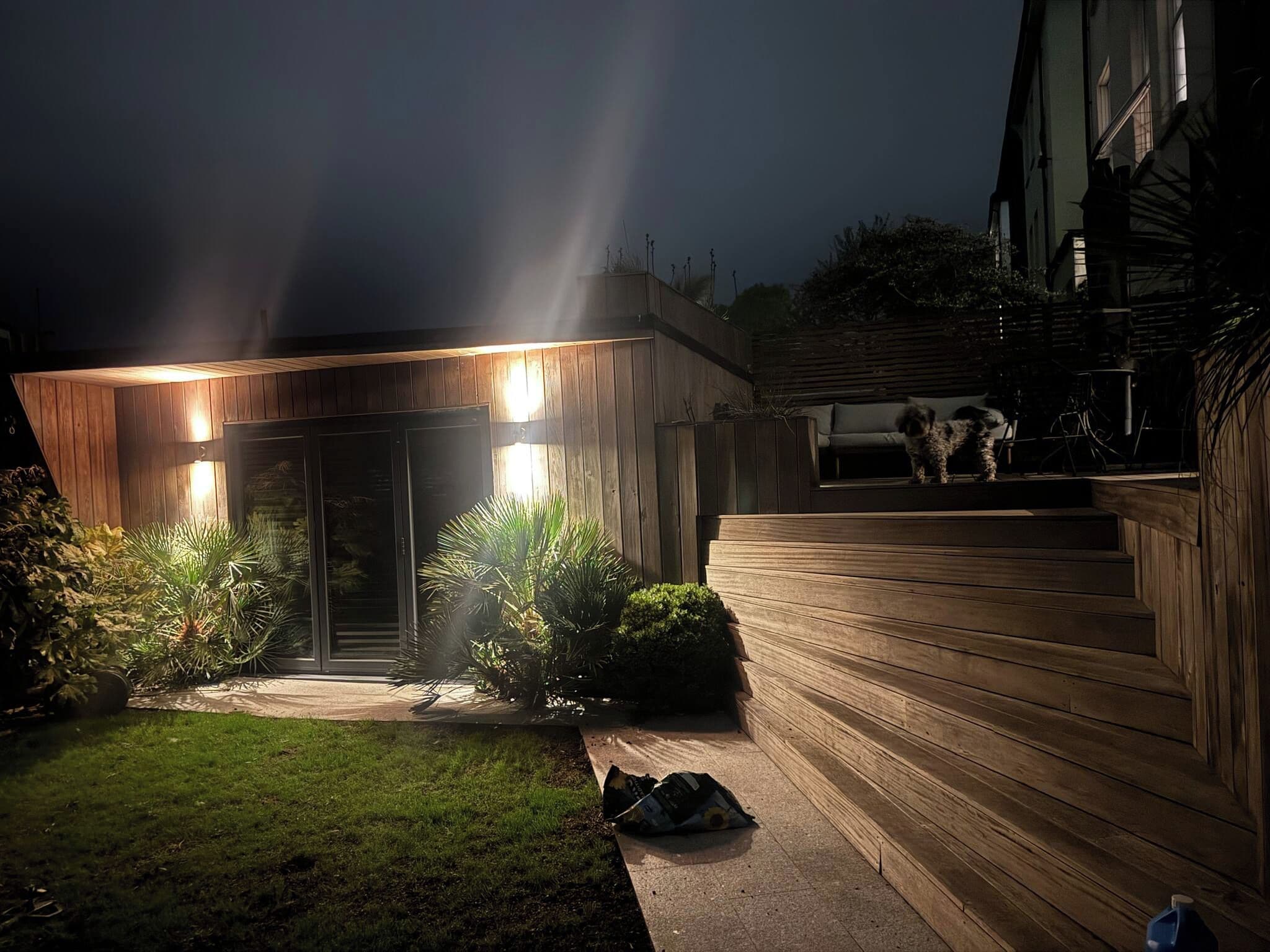 Una casa moderna con fachada de madera, puerta de cristal y un patio delantero bien iluminado.