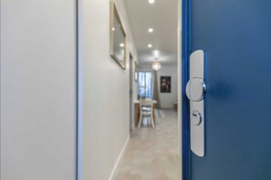Un pasillo con una puerta azul, una pared blanca e iluminación empotrada en el techo.