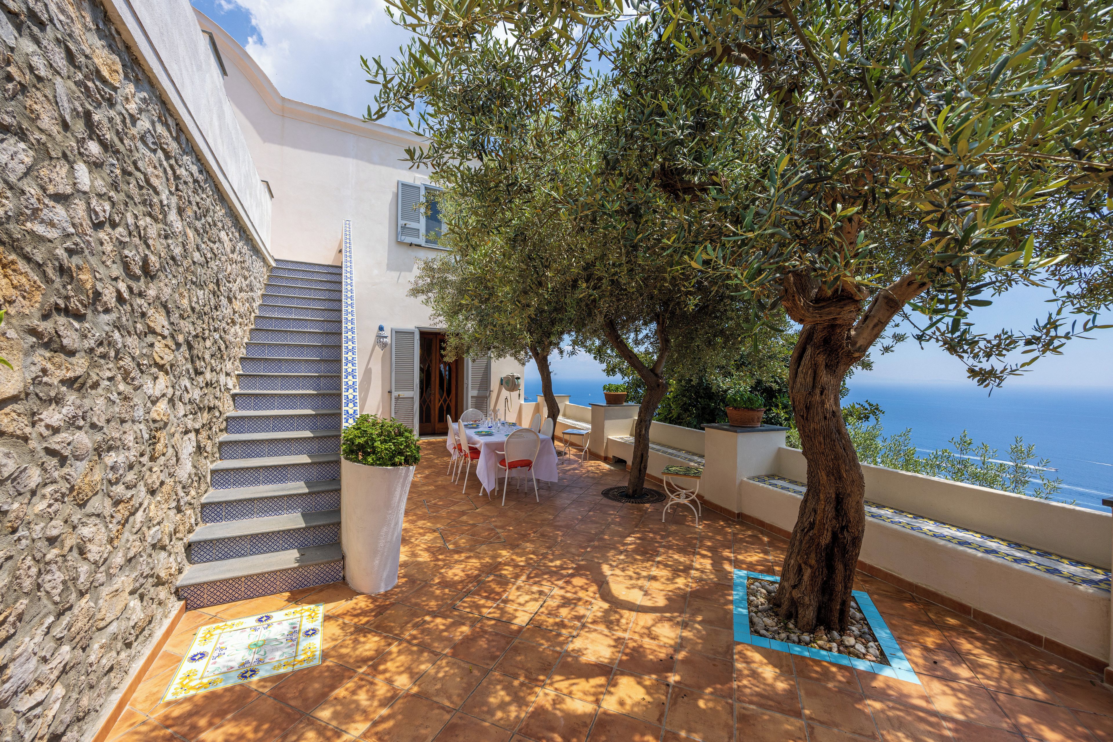 Eine Terrasse mit einer Steinmauer, einem Baum und Blick auf das Meer.