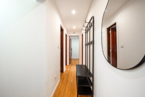 A hallway with a wooden floor, a black metal bench, and a wall-mounted mirror. - GuestReady-Charming Lisbon Retreat (Lisbon)