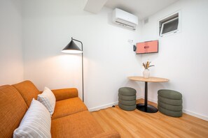 Une pièce moderne comprenant un canapé, une lampe sur pied, une petite table avec un vase et un climatiseur fixé au mur.