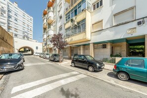Straßenansicht mit mehrstöckigen Wohnhäusern, parkenden Autos und einer Fußgängerzone.