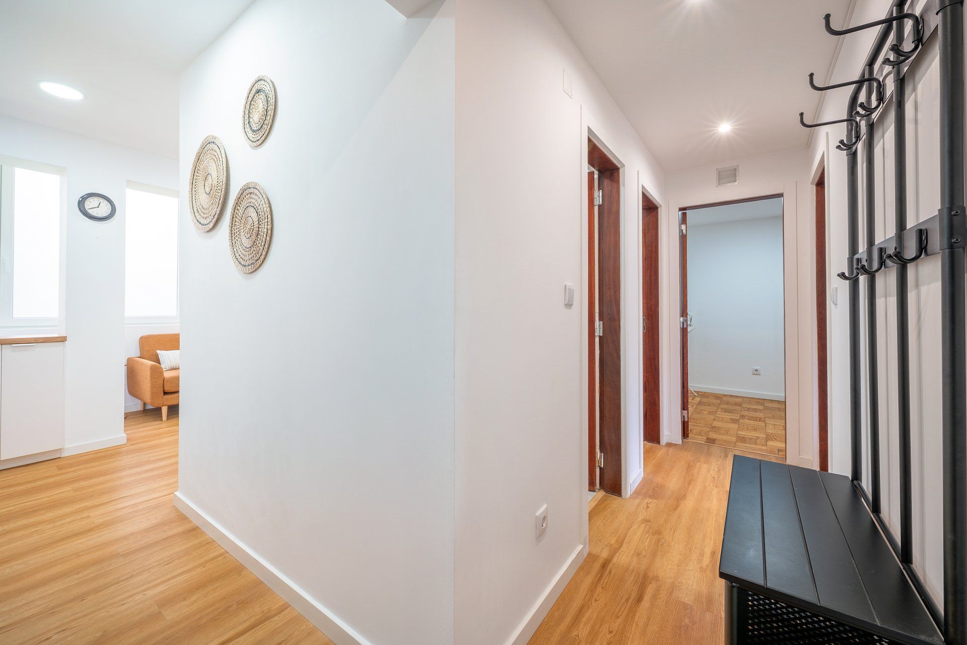A hallway with a bench, a coat rack, and a door leading to another room.