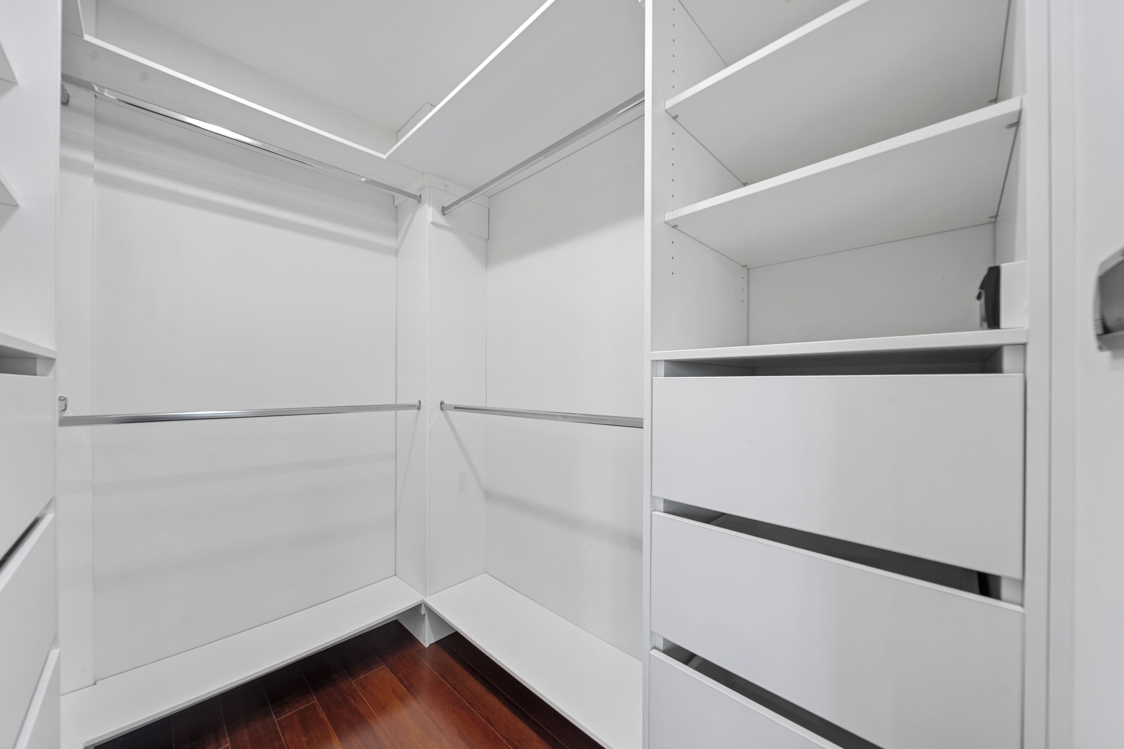 A walk-in closet with white shelving units and a wooden floor.