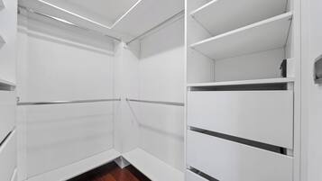 A walk-in closet with white shelving units and a wooden floor.