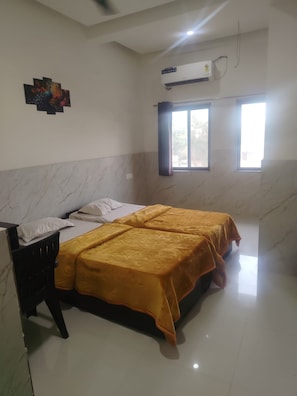 A room with two beds, a desk, an air conditioning unit, and a window with curtains.