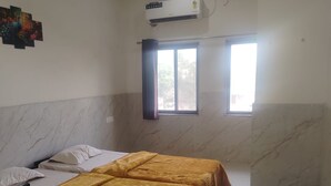 Una habitación de hotel con cama, ventilador de techo, equipo de aire acondicionado y ventana con cortinas.