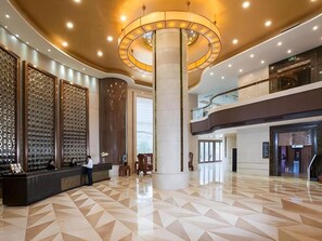 A spacious lobby with a reception desk, a large central column, and a modern ceiling design.