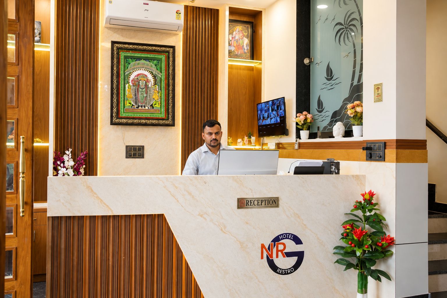 A hotel reception desk with a marble counter, a framed religious painting, a television, and a logo for 'Hotel NRG Restro'.