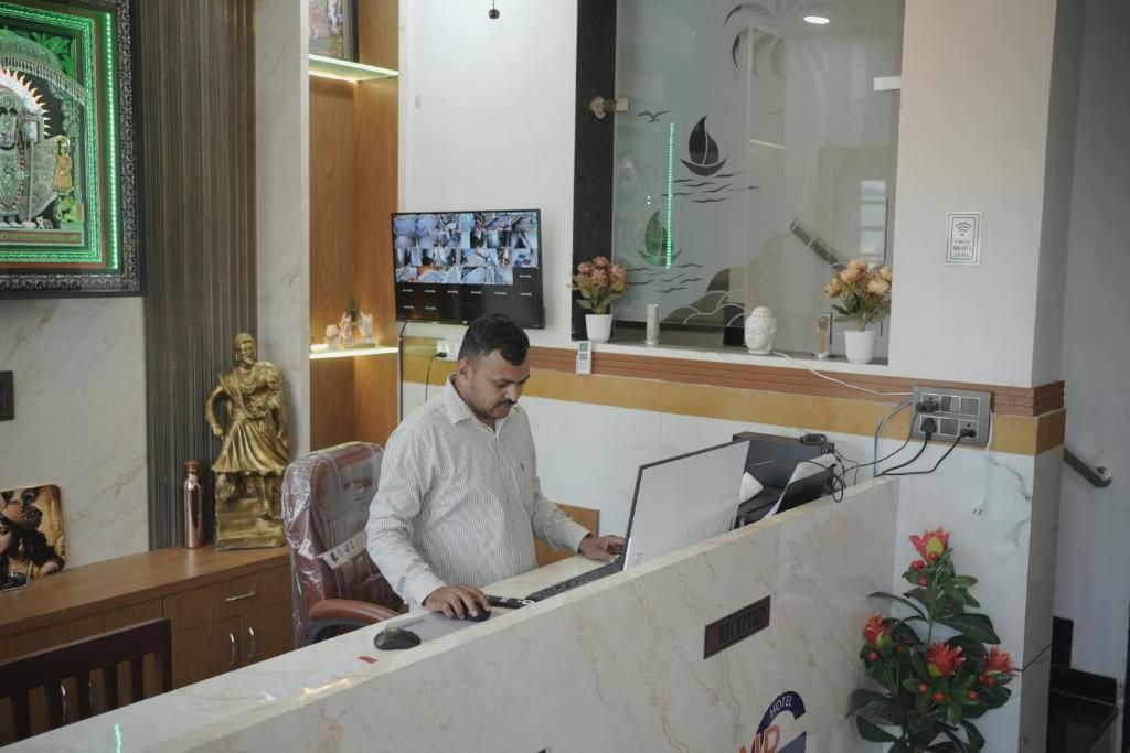 A reception desk with a computer, a monitor displaying multiple screens, and a statue.