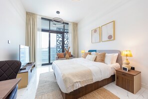 Ein modernes Hotelzimmer mit einem großen Bett, einem Schreibtisch, einem Sessel, einem Fernseher und einem Balkon mit Blick.