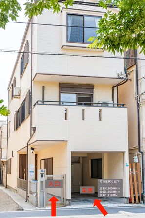 A multi-story residential building with a ground-level entrance, a visible car storage area, and a balcony on the upper floor. - Saraisora Suminoe (Osaka)