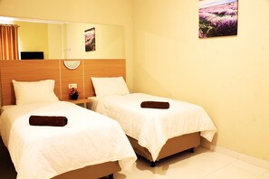 Een hotelkamer met twee bedden, een nachtkastje met een lamp, een spiegel en een schilderij aan de muur.