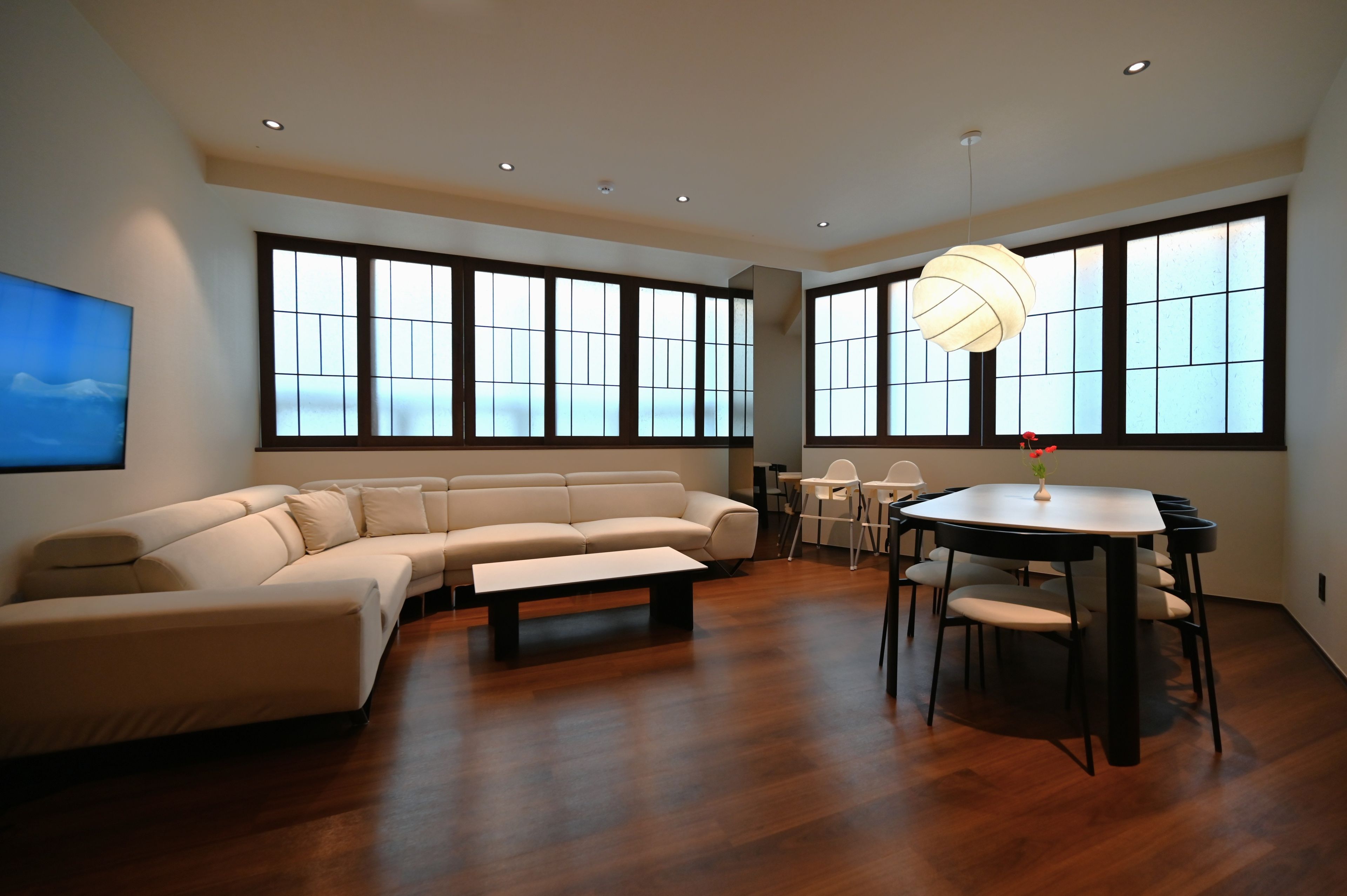 A modern living room with a sectional sofa, a dining table with chairs, and large windows with frosted glass panels.