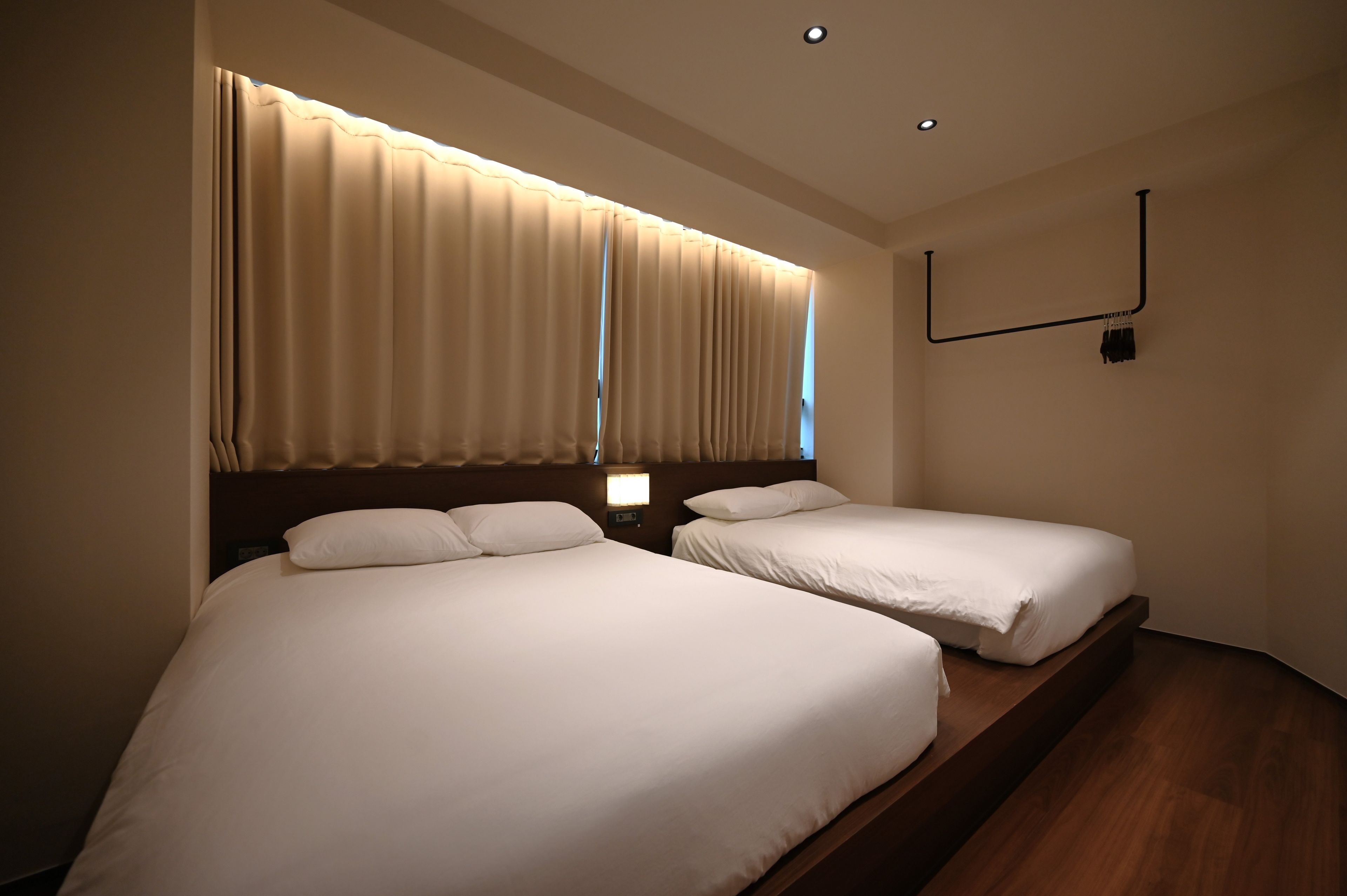 A hotel room with two beds, a nightstand, a wall-mounted TV, and a ceiling light.