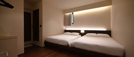 Habitación de hotel con dos camas, un ventanal con cortinas, suelo de madera e iluminación empotrada en el techo.