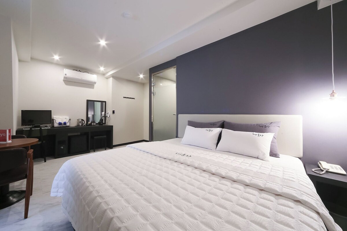 Une chambre d’hôtel avec un grand lit, un bureau avec un ordinateur, un miroir et une table de chevet avec un téléphone.