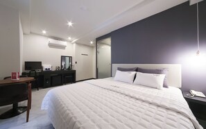 Une chambre d’hôtel avec un grand lit, un bureau avec un ordinateur, un miroir et une table de chevet avec un téléphone.