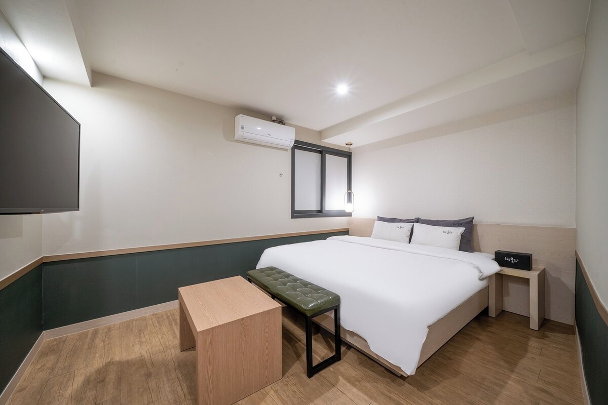 Une chambre d’hôtel équipée d’un lit, d’une banquette, d’une table de chevet, d’un téléviseur et d’un appareil de climatisation.
